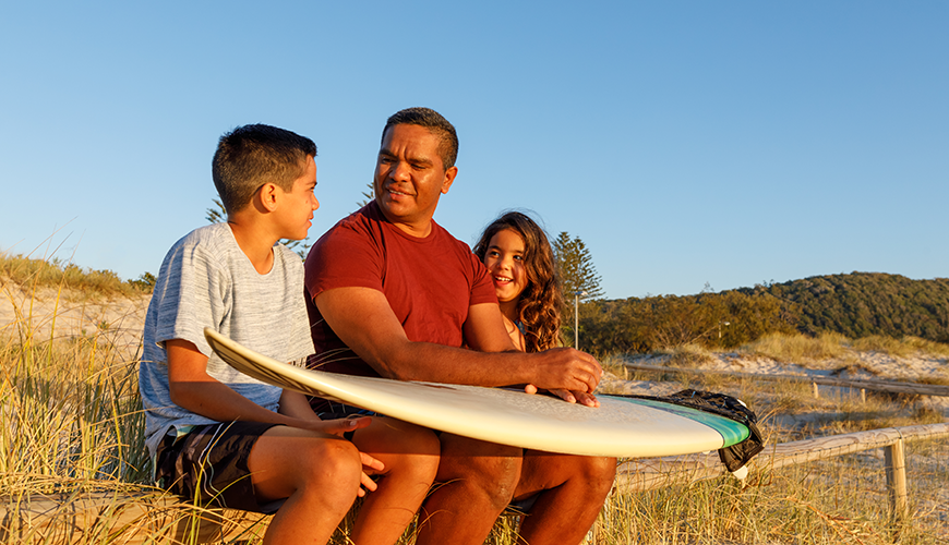 iStock-1025084848_870x500.png Aboriginal father talking to his children at the beach