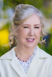 headshot of woman with long grey hair pulled up and back wearing white coat