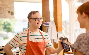 A young person with a disability wears an apron and serves a customer at a