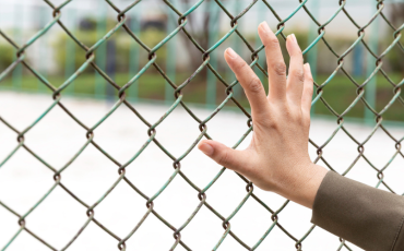 A woman's hand holds onto the wired fence inside a detention facility