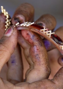 Close-up of two hands with dirty, stained fingers carefully holding an ornate, gold-decorated bangle.